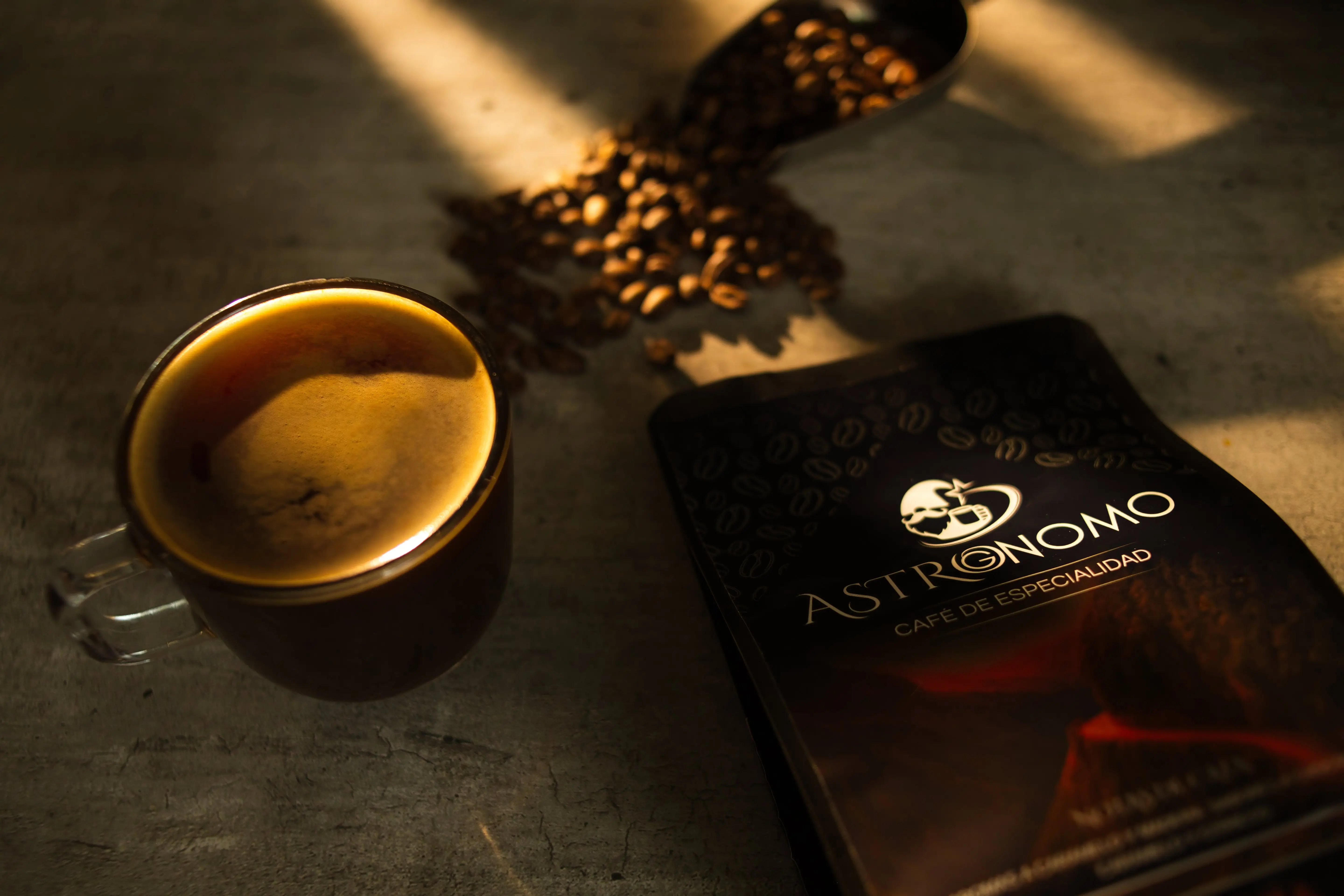 Taza de espresso recién hecha junto a una bolsa de café Astrognomo iluminada con luz dorada
